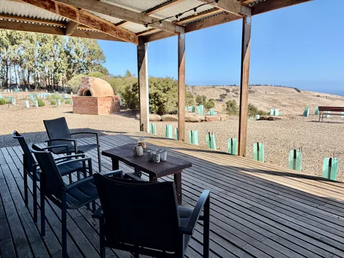 Covered deck with dining table and pizza oven, overlooking the restoration site