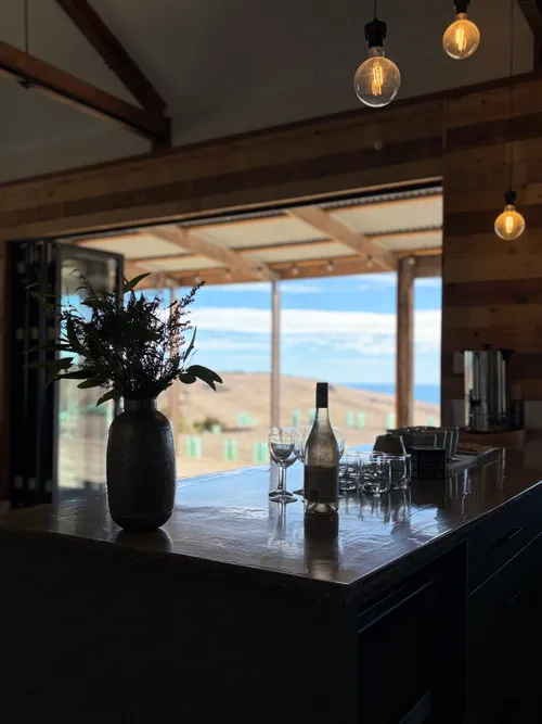 Kitchen bench with a wine bottle, glasses and an ocean view through open doors